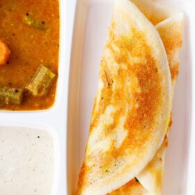 folded masala dosa in a white partitioned tray with sambar and coconut chutney