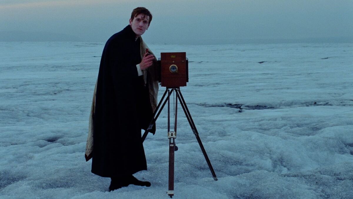 A man sets up a camera on an icy, flat landscape.