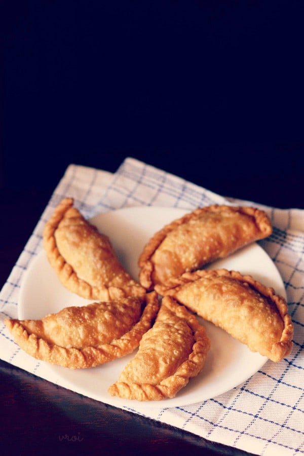 gujiya arranged neatly on a white plate placed on a white and blue checkered napkin