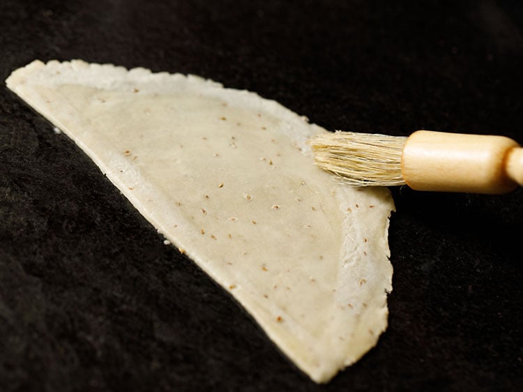 half of the cut dough being rolled lightly with a wooden rolling pin