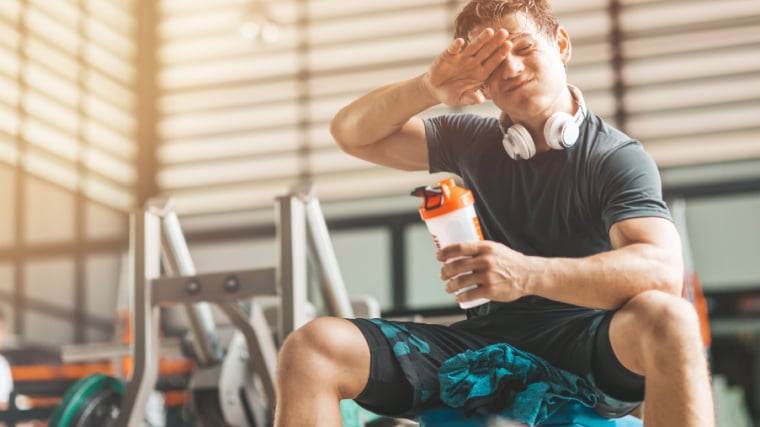 Person in gym sweating drinking pre-workout.