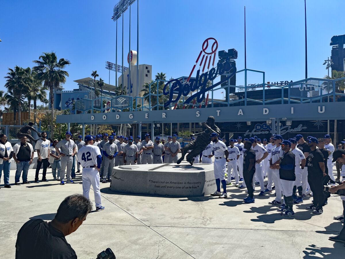 Dodgers manager Dave Roberts speaks as Dodgers and Chicago Cubs players gather around a statue of Jackie Robinson.