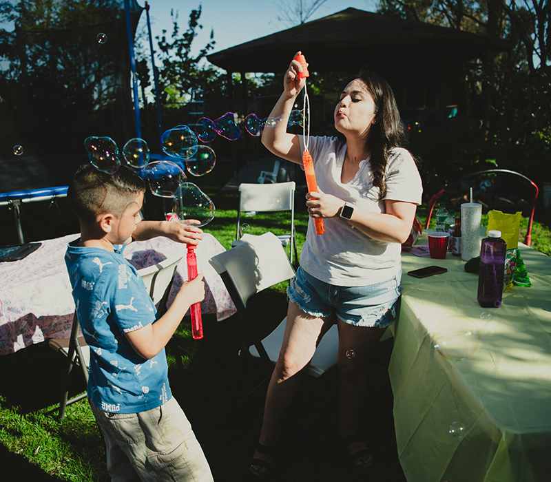Ms. Rodríguez blows bubbles with her young son during a backyard family party.