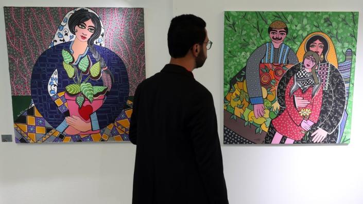 A man stands between two paintings in a gallery (on the left is a painting of woman; on the right is a painting of a man, woman and child) in Tunis, Tunisia - Saturday 27 May 2023