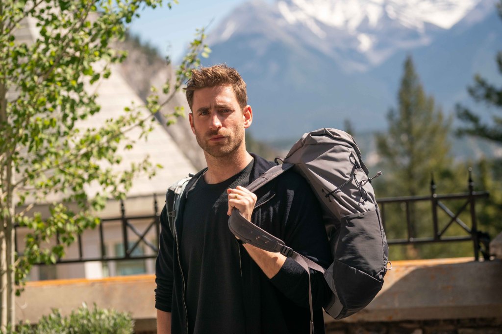 Oliver Jackson-Cohen wearing a backpack standing outside. 