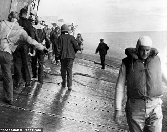 A scene on the flight deck of USS Yorktown shortly after it was hit by two Japanese aerial torpedoes. Men are balancing themselves on the listing deck as they prepare to abandon ship.
