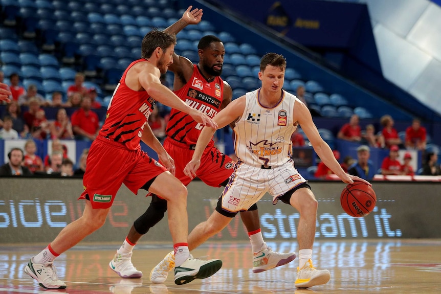 A male basketball player bounces the ball as he plays against two defenders in the NBL grand final series.