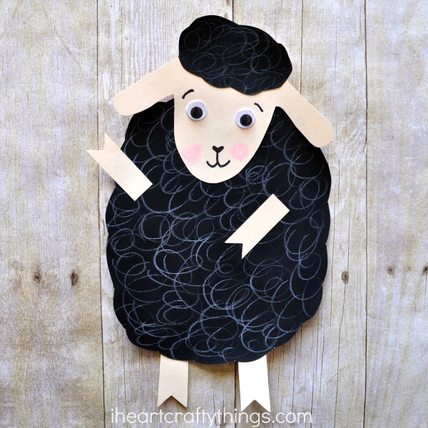 A sheep has a large black body cut out of construction paper. It also has a face, ears, legs, and arms made from peach colored construction paper.