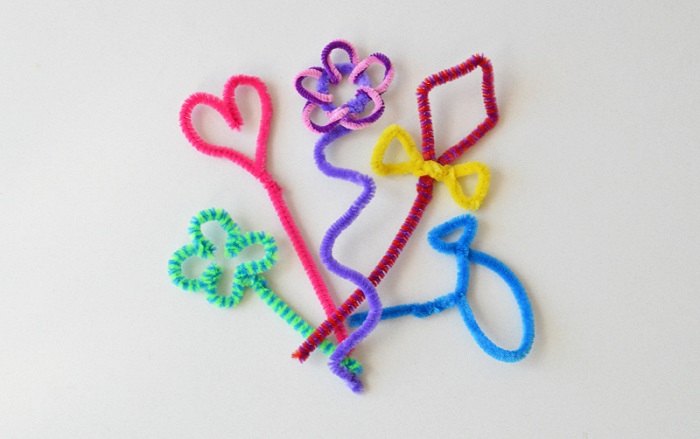 Several different color pipe cleaners are bent into different shapes including a diamond, fish, flower, and heart. Example of easy crafts for kids.