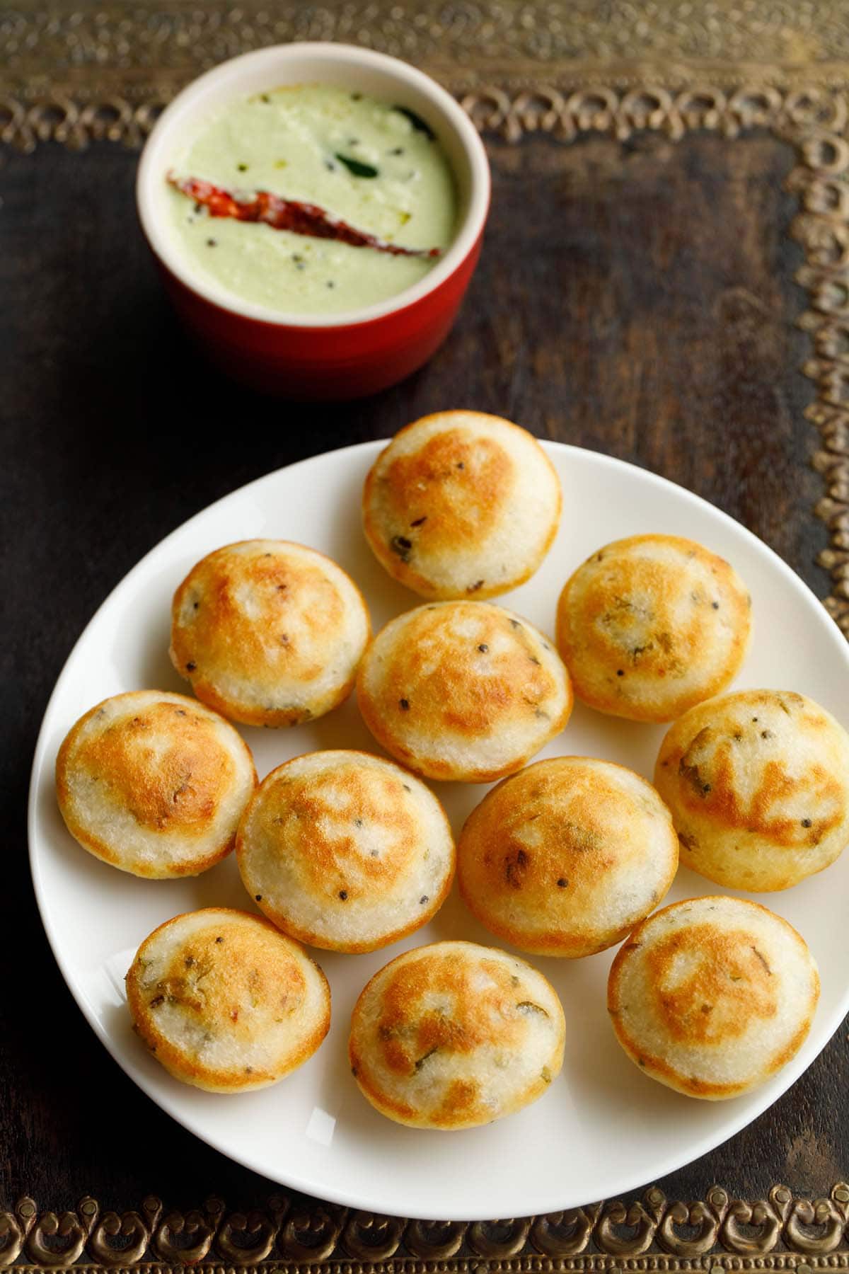 appe on a plate with coconut chutney in red bowl on top.