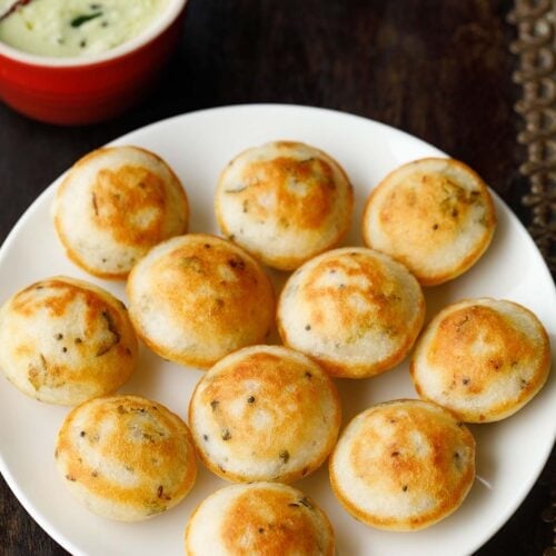 appe or paddu on a plate with coconut chutney in red bowl on top.