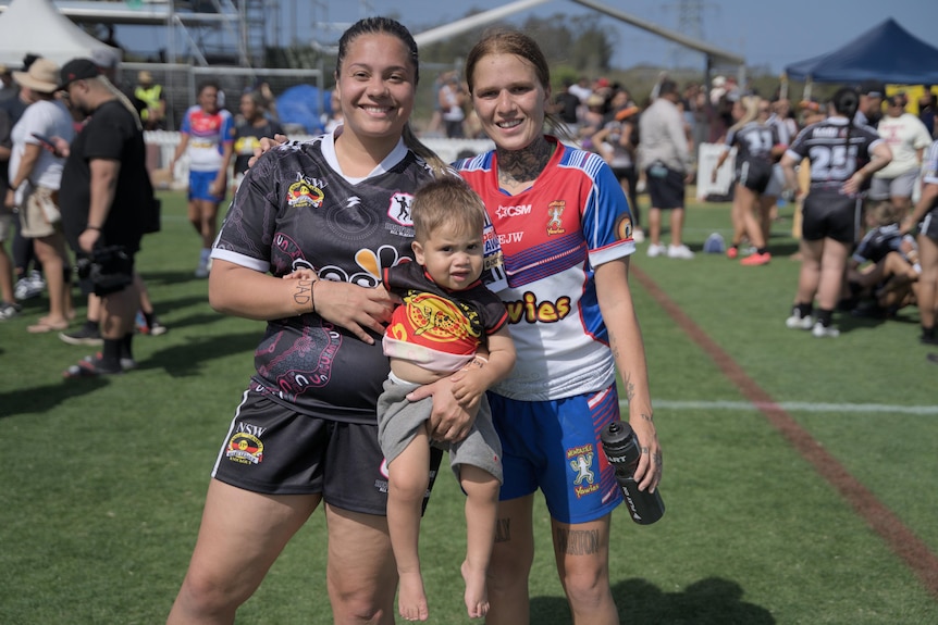 two women, rugby league players, stand together for a photo with a young boy