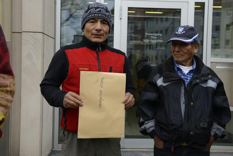 Two Peruvian men outside a courthouse, one holding a large envelope.