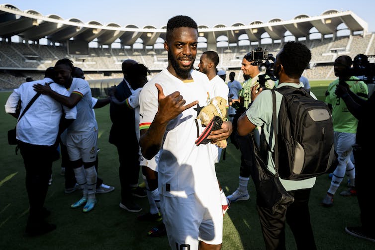 A Ghanaian footballer on the pitch looking directly at the camera celebrating.