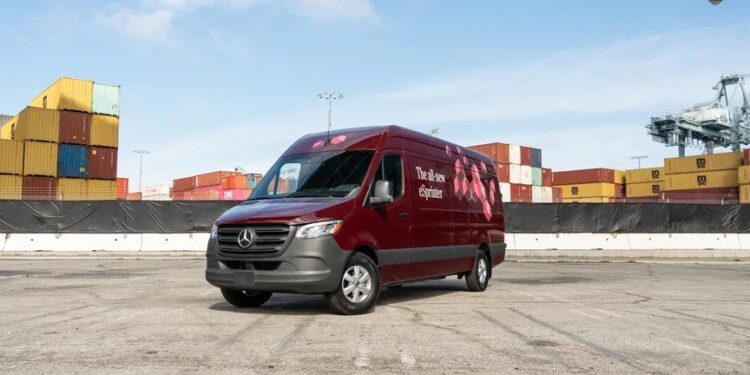 A maroon van sits in an empty lot in front of shipping containers