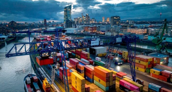 Containers being loaded onto a cargo ship in Frankfurt, Germany, with a view of the city and the European Central Bank in the background