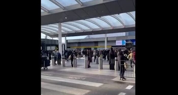 A crowd of passengers standing outside under a covered area at Gatwick airport