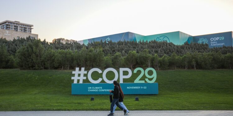 Citizens walks near a sign for COP29 near the Baku Olympic Stadium, the venue of the COP29 United Nations Climate Change Conference on October 23, 2024 in Baku, Azerbaijan.