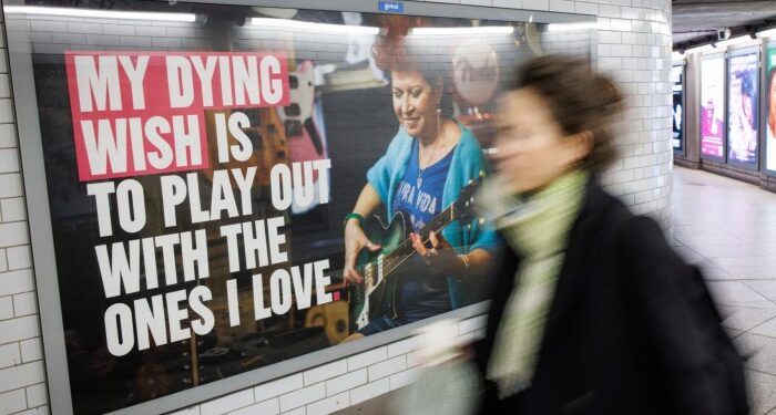 Pedestrians walk past the posters promoting the Assisted Dying bill at Westminster Underground station