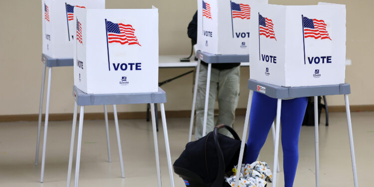 A photo of two voters â€” a man in the back and a woman with a baby carrier in the front.