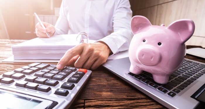 A person using a calculator with a piggy bank in the foreground.