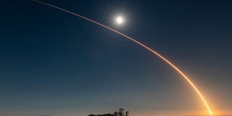 A rocket launch carves an orange arc into a dark night sky in this long-exposure photo.