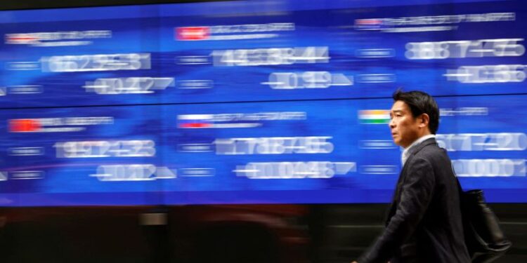 © Reuters. FILE PHOTO: A passerby walks past an electric monitor displaying various countries' stock price index outside a bank in Tokyo, Japan, March 22, 2023. REUTERS/Issei Kato/File Photo