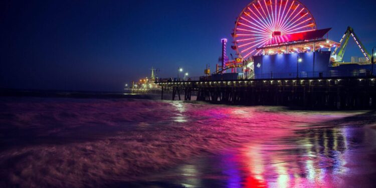 Nighttime beach scene with pier in the background atop which are amusements and illuminated big wheel