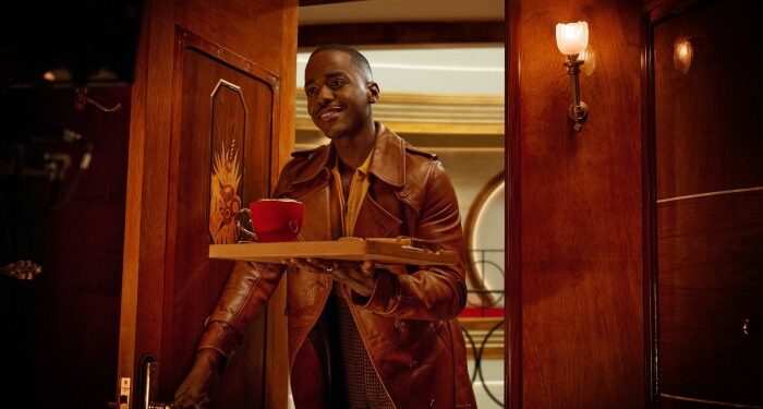 a man entering a room with a friendly demeanour, holding a tray with a red cup and saucer