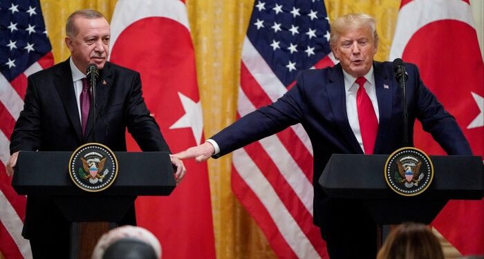 Donald Trump and Recep Tayyip Erdoğan standing at podiums, with Trump touching Erdoğan ‘s hand