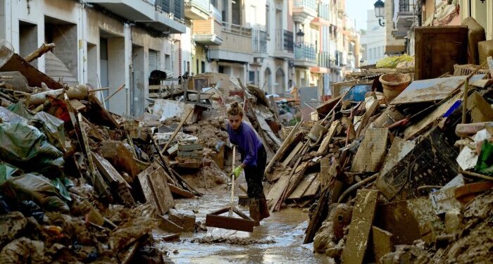 A woman works to clean mud among debris in a street of Paiporta, south of Valencia