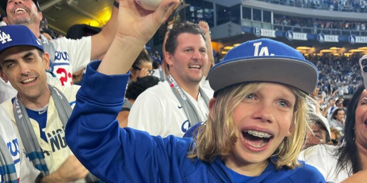 Zachary Ruderman holds up a baseball and smiles in the stands.