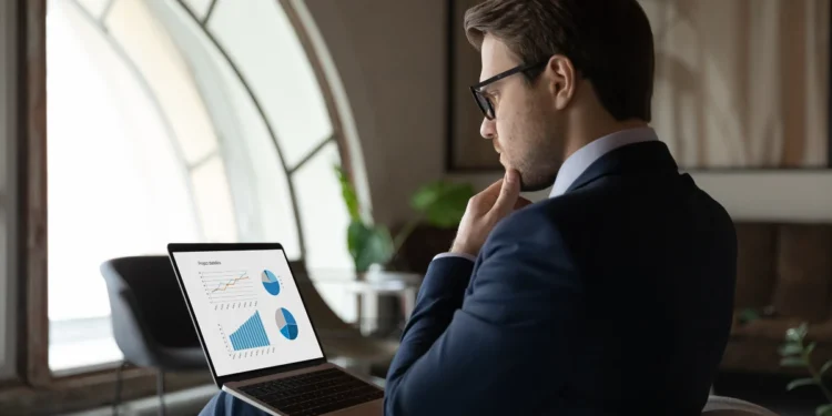 Businessman looking at graphs on a laptop screen, apparently lost in thought