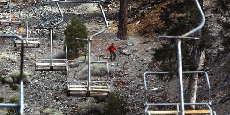 A hiker makes his way down a slope lined with ski lifts.