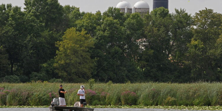 Two fishermen in a boat on a lake near a farm.