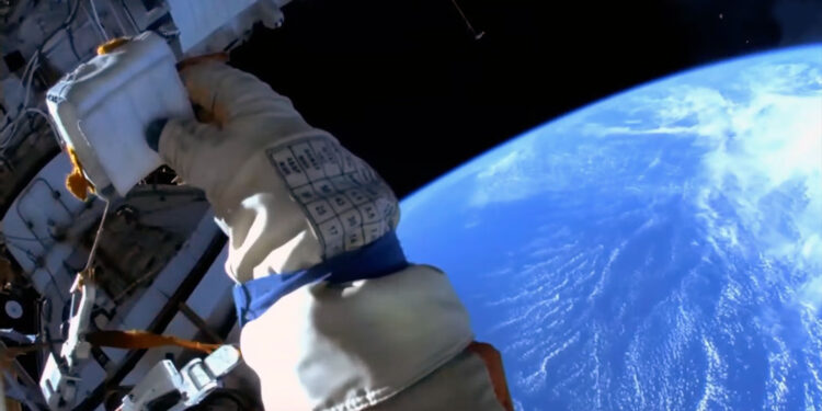 A cosmonaut's gloved hand is seen against the Earth below as viewed from a spacesuit helmet-mounted camera during a spacewalk.