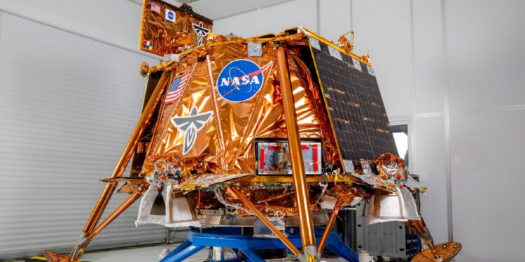 a cube-shaped spacecraft covered in gold foil sits on a dolly in a white cleanroom