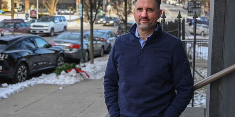 A man in a blue zip up sweater stands on a city street