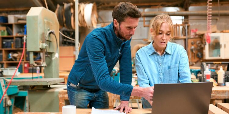 Man and young woman looking at laptop, wearing casual clothes, in workshop-like space