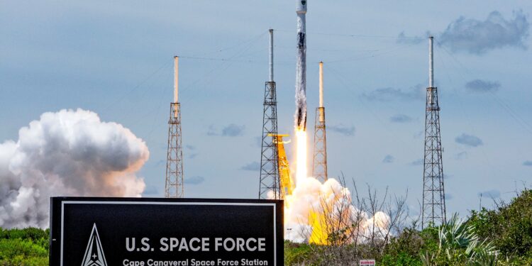 a white rocket lifts off behind a large sign that reads