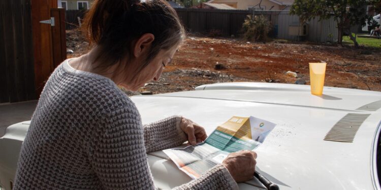 A woman reads a flier on the hood of an automobile.