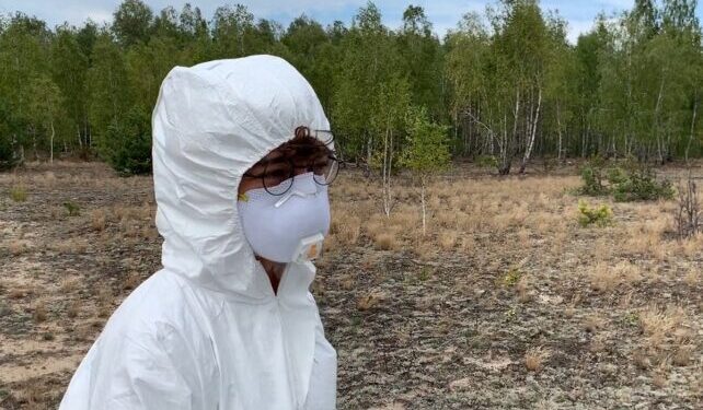 A person wearing PPE, standing in a field