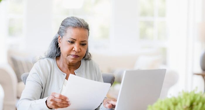 Serious person looking at documents while sitting at laptop.