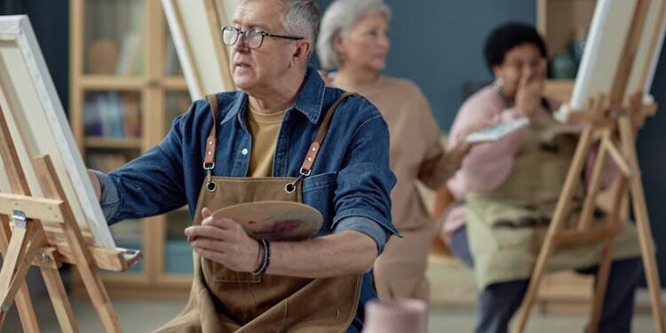 Older man applying paint to a canvas as part of an art class